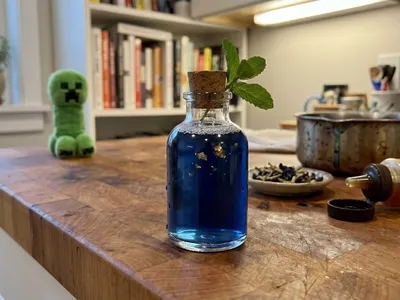 My Caver's Draught — deep indigo flask with gold flakes, a Creeper plush set back at the far edge