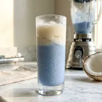 My Binary Sunset — frozen blue-and-cream layered cocktail, Luke's lightsaber hilt at the edge of the frame